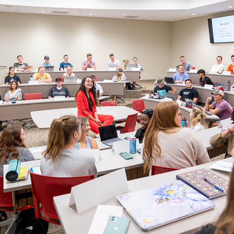 Female professor smiles as she listens to a students comment in tiered classroom.
